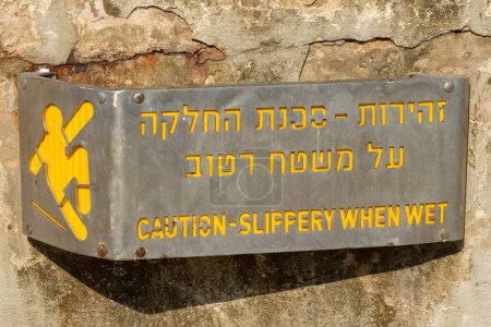 Foto de Tel Aviv, Israel septiembre 9, 2022 Precaución resbaladiza cuando está mojado letrero de metal con letras amarillas en hebreo e inglés en Israel. - Imagen libre de derechos