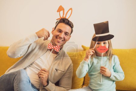 Foto de Padre e hija divirtiéndose con accesorios de fiesta en su casa. - Imagen libre de derechos