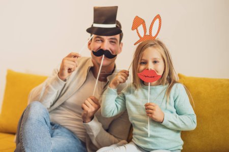 Foto de Padre e hija divirtiéndose con accesorios de fiesta en su casa. - Imagen libre de derechos