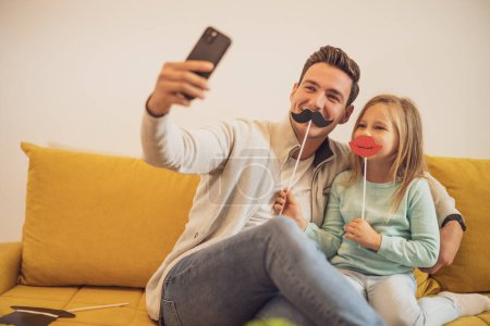 Photo for Father and daughter taking selfie while they  having fun with  party props at their home. - Royalty Free Image