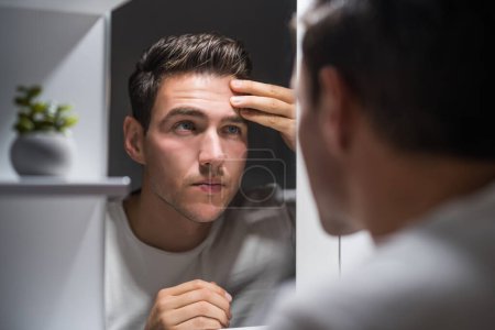 Téléchargez les photos : Man looking at his wrinkles while standing in front of mirror. - en image libre de droit
