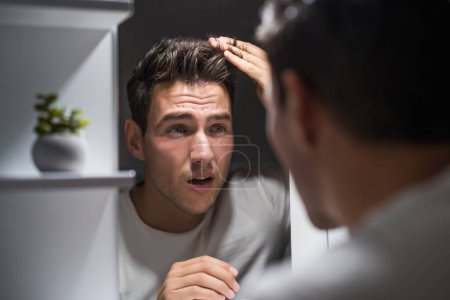 Téléchargez les photos : Worried man is looking his hair in the mirror. - en image libre de droit
