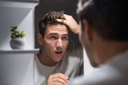 Foto de Worried man is looking his hair in the mirror. - Imagen libre de derechos