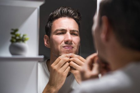 Photo for Man squeezing pimple while looking himself in the mirror. - Royalty Free Image