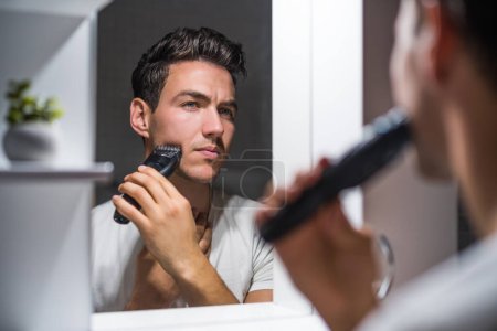 Téléchargez les photos : Man shaving  beard while looking himself in the mirror. - en image libre de droit