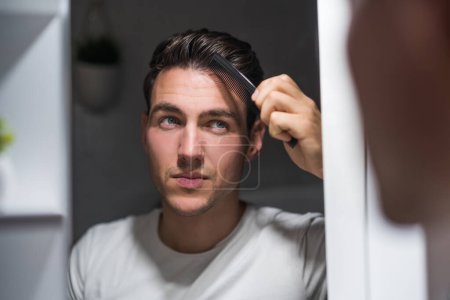 Téléchargez les photos : Man combing his hair while looking himself in the mirror. - en image libre de droit