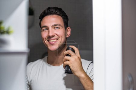 Téléchargez les photos : Man using deodorant  while looking himself in the mirror. - en image libre de droit