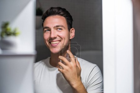 Photo for Man using perfume while looking himself in the mirror. - Royalty Free Image