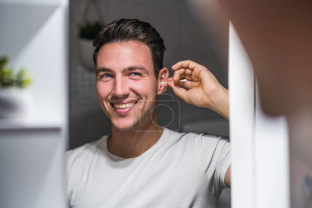 Téléchargez les photos : Man cleaning ear while looking himself in the mirror. - en image libre de droit