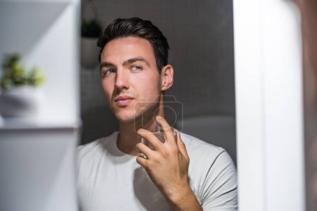 Téléchargez les photos : Man using perfume while looking himself in the mirror. - en image libre de droit
