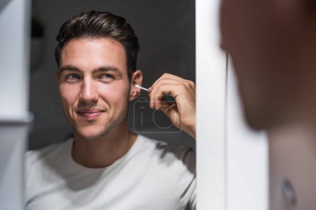 Photo for Man cleaning ear while looking himself in the mirror. - Royalty Free Image