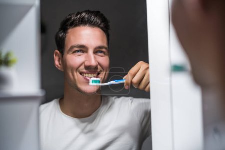 Téléchargez les photos : Man is  brushing teeth while looking himself in the mirror. - en image libre de droit