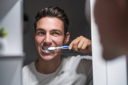 Téléchargez les photos : Man is  brushing teeth while looking himself in the mirror. - en image libre de droit