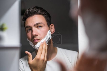 Foto de Man applying shaving cream while looking himself in the mirror. - Imagen libre de derechos