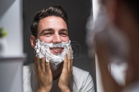 Téléchargez les photos : Man applying shaving cream while looking himself in the mirror. - en image libre de droit