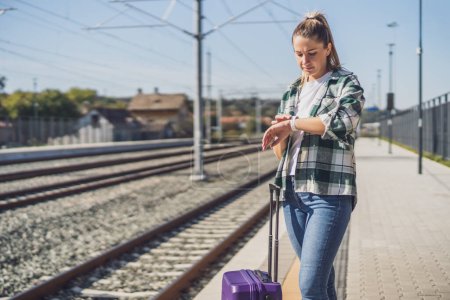 Téléchargez les photos : Femme regardant son horloge debout avec une valise sur une gare. - en image libre de droit
