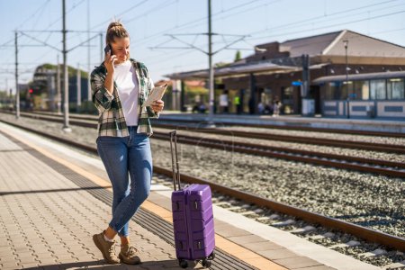 Photo for Happy woman using mobile phone and holding map on a train station. - Royalty Free Image