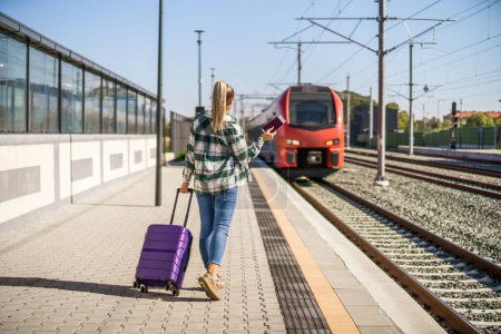 Foto de Mujer con maleta sosteniendo billete y esperando para entrar en el tren en la estación. - Imagen libre de derechos