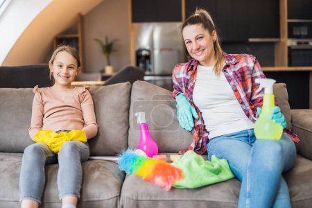 Téléchargez les photos : Mère et fille heureuses se reposant après avoir nettoyé leur maison ensemble. - en image libre de droit