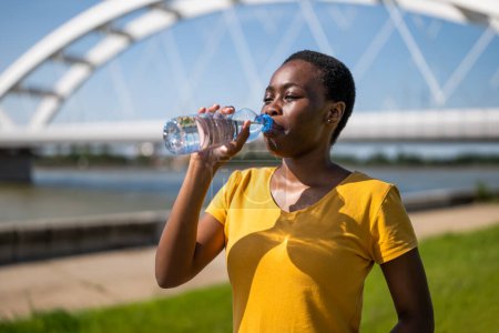 Foto de Deportiva mujer bebiendo agua mientras hace ejercicio al aire libre. - Imagen libre de derechos