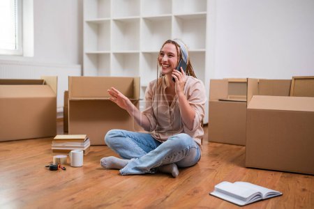 Photo for Modern ginger woman with braids talking on the phone while moving into her new apartment. - Royalty Free Image