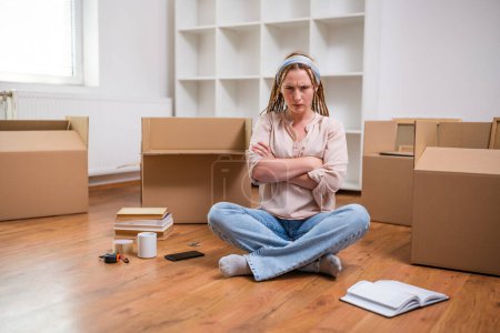 Photo for Angry ginger woman with braids sitting on the floor in new apartment. She is exhausted of moving . - Royalty Free Image