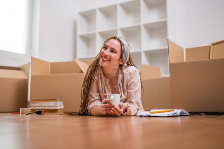Photo for Modern ginger woman with braids  drinking coffee while moving into her new apartment. - Royalty Free Image