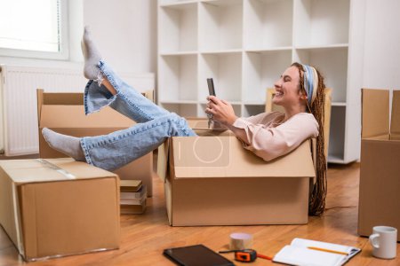 Photo for Happy woman using phone and having fun while moving into new apartment. - Royalty Free Image