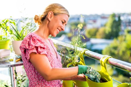 Happy woman enjoys in  gardening on balcony at her home. She is putting soil into flower pot.