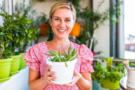 Téléchargez les photos : Femme heureuse jardinage sur le balcon à la maison. Elle regarde la croissance de sa plante succulente. - en image libre de droit