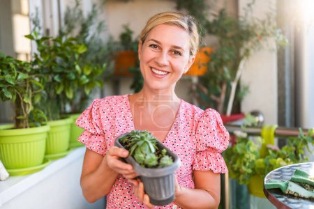 Foto de Mujer feliz jardinería en el balcón en casa. Ella está buscando el crecimiento de su planta casera. - Imagen libre de derechos