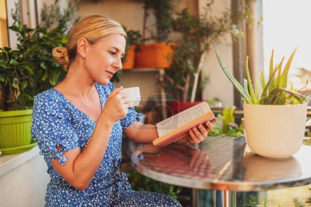 Foto de Hermosa mujer disfruta leyendo libro y tomando café en su balcón. - Imagen libre de derechos