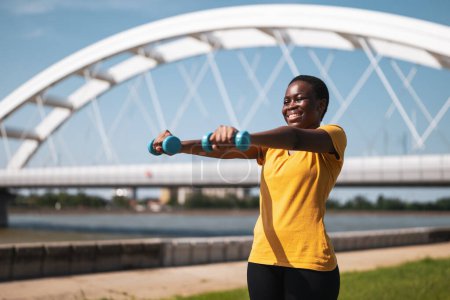 Foto de Mujer joven disfruta haciendo ejercicio con pesas al aire libre. - Imagen libre de derechos