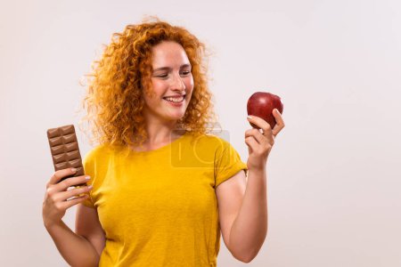 Foto de Hermosa mujer de jengibre está sosteniendo manzana y chocolate. Ella ha decidido comer sano. - Imagen libre de derechos