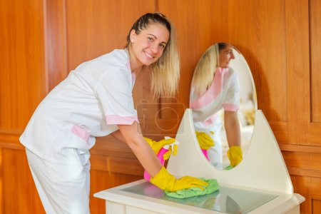 Foto de Hermosa mucama de hotel limpiando muebles en una habitación. - Imagen libre de derechos