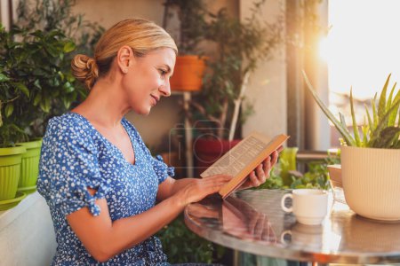 Téléchargez les photos : Belle femme aime lire le livre et boire du café sur son balcon. - en image libre de droit
