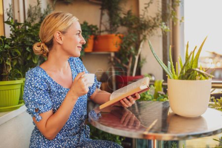 Téléchargez les photos : Belle femme aime lire le livre et boire du café sur son balcon. - en image libre de droit