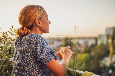 Téléchargez les photos : Belle femme aime boire du café tout en se tenant sur son balcon au coucher du soleil. - en image libre de droit