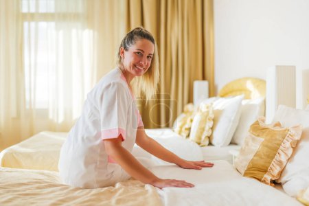 Téléchargez les photos : Belle femme de chambre d'hôtel faisant le lit dans une chambre. - en image libre de droit