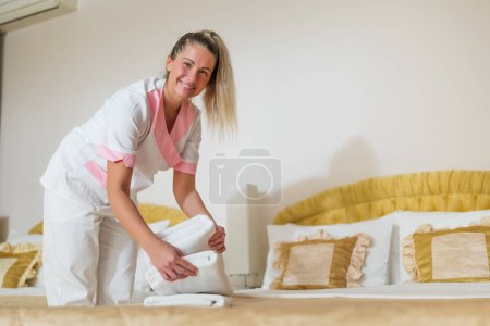 Photo for Beautiful hotel maid putting fresh and clean towels on bed in room. - Royalty Free Image