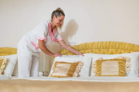 Photo for Beautiful hotel maid  making bed in a room. - Royalty Free Image