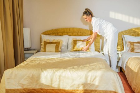 Téléchargez les photos : Belle femme de chambre d'hôtel faisant le lit dans une chambre. - en image libre de droit