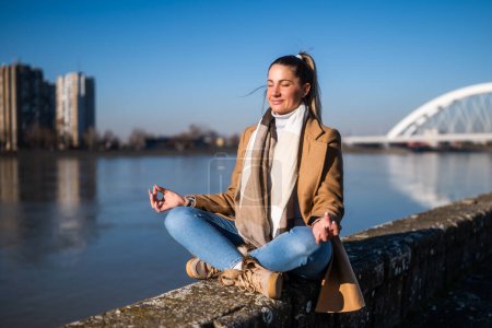 Téléchargez les photos : Belle femme aime méditer au bord de la rivière par une journée d'hiver ensoleillée. - en image libre de droit