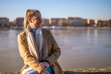 Téléchargez les photos : Belle femme en vêtements chauds aime se reposer au bord de la rivière par une journée d'hiver ensoleillée. Image tonique. - en image libre de droit