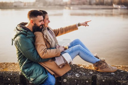 Téléchargez les photos : Couple heureux embrassant tout en appréciant assis au bord de la rivière. - en image libre de droit