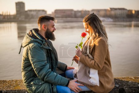Foto de Hombre dando rosa roja a su mujer mientras disfrutan pasar tiempo juntos al aire libre. - Imagen libre de derechos