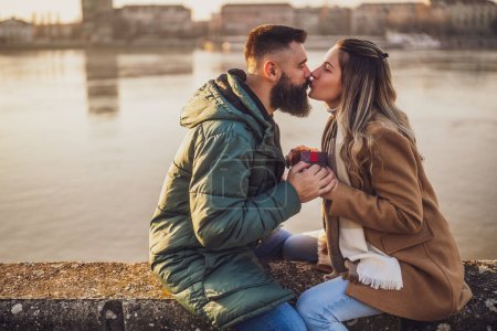 Foto de Feliz pareja besos mientras hombre dando regalos a su mujer al aire libre. - Imagen libre de derechos