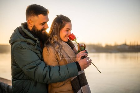 Téléchargez les photos : Homme heureux donnant rose rouge à sa femme alors qu'ils aiment passer du temps ensemble sur un coucher de soleil. - en image libre de droit