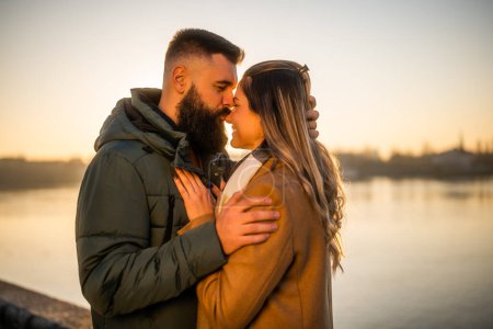 Téléchargez les photos : Heureux couple profiter de passer du temps ensemble en plein air sur un coucher de soleil. L'homme embrasse sa femme dans le nez. - en image libre de droit