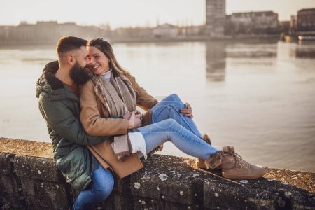 Téléchargez les photos : Couple heureux embrassant tout en appréciant assis au bord de la rivière. - en image libre de droit